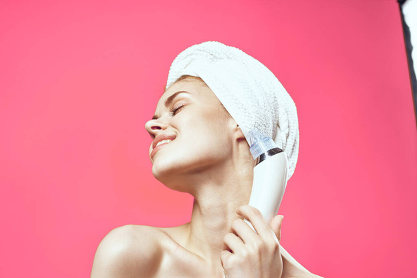 cheerful woman with a towel on her head vacuum face cleaning pink background - Photo, Image