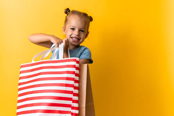 Portrait Caucasian Beautiful Happy Little Preschool Girl Smiling Cheerful And Holding Cardboard Bags Isolated On Orange Yellow Studio background. Happiness, Consumerism, Sale People shopping Concept - Foto, Imagen