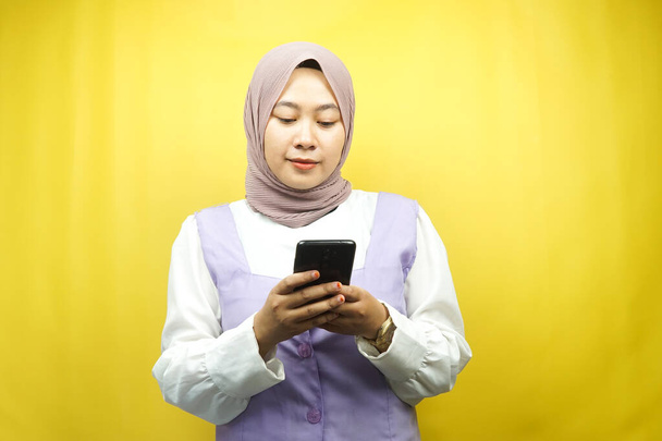 Hermosa asiática joven musulmana sosteniendo teléfono inteligente aislado sobre fondo amarillo - Foto, Imagen