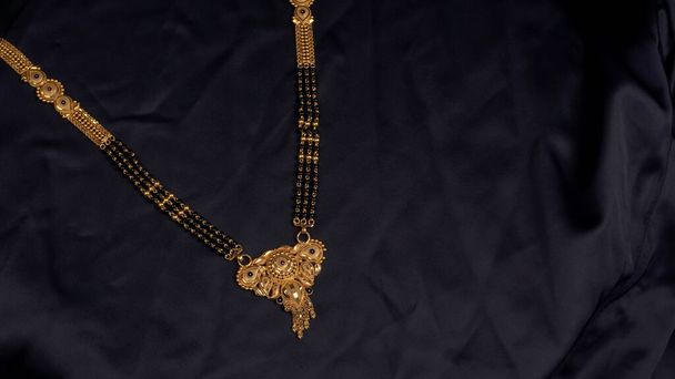 Mangalsutra lub Złoty Naszyjnik do noszenia przez zamężne hinduskie kobiety, ułożone na czarnym tle. Indyjska tradycyjna biżuteria. - Zdjęcie, obraz
