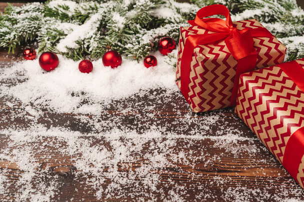 Presents on wooden background with fir tree branches and red baubles powdered with snow - Fotografie, Obrázek