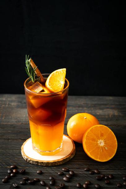 Sklenice ledové americké černé kávy a vrstva pomerančové a citrónové šťávy zdobené rozmarýnem a skořicí - Fotografie, Obrázek