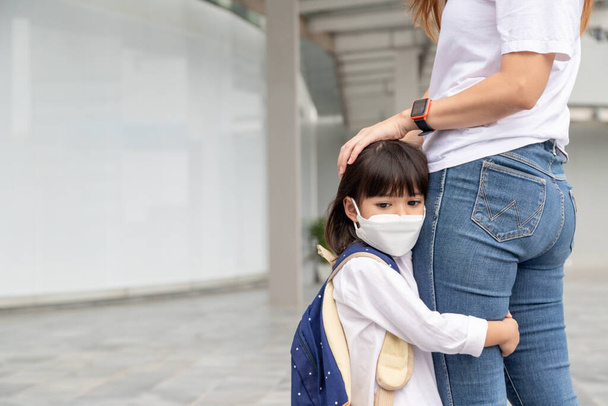 mother accompanies the child to school. mom supports and motivates the student. the little girl wearing a face mask does not want to leave her mother. fears primary school. - Photo, Image