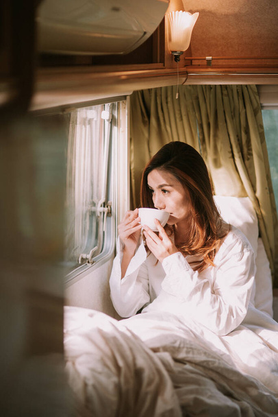 ráno, útulnost, zima a lidé koncept - zblízka šťastná mladá žena s šálkem kávy nebo kakaového nápoje v posteli - Fotografie, Obrázek