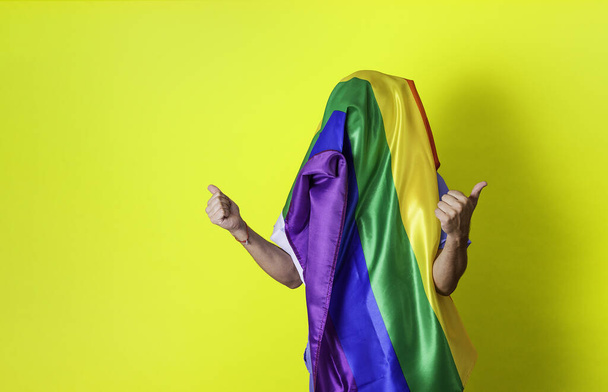 Unrecognizable person with LGBTIQ flag covering his head. Gay pride concept. Yellow background with copy space. - Foto, immagini