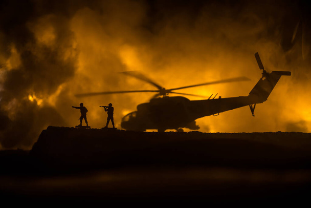 A katonai helikopter sziluettje készen áll a harci zónából való repülésre. Díszített éjszakai felvétel helikopterrel kezdődik a sivatagban ködös tónusú háttérvilágítással. Szelektív fókusz. Háborús koncepció - Fotó, kép