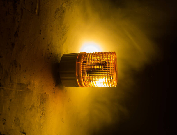 Vészvilágítás a gyárban, figyelmeztető fény, narancssárga sziréna a betonfalon. Forgó sziréna. - Fotó, kép