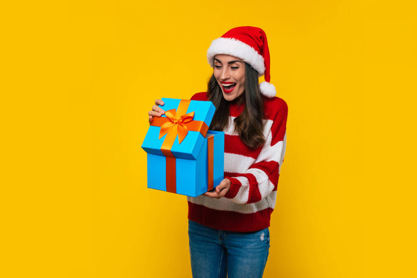 Close up photo of beautiful excited smiling woman with Christmas gift box in hands is having fun while posing on yellow background  - Fotografie, Obrázek