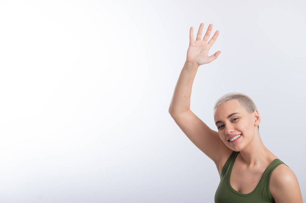 Young Caucasian Woman Holding Raised Hand White Background Smiling Girl Green Tshirt Short Blond Hair. - Фото, зображення