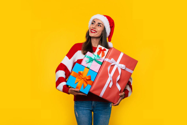Close up photo of beautiful excited smiling woman with many cool Christmas gift boxes in hands while she is having fun and posing on yellow background  - Foto, Bild