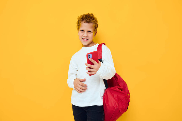 sorridente ragazzino con uno zaino rosso chiama sullo sfondo giallo del telefono - Foto, immagini