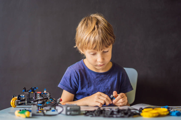 Cheerful smart schoolboy sitting at the table and constructing a robotic device at home - Фото, зображення