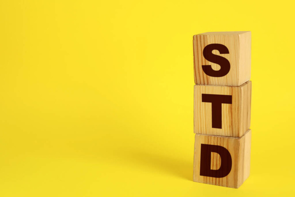 Abbreviation STD made with wooden cubes on yellow background, space for text - Фото, изображение