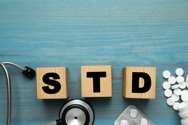 Abbreviation STD made with cubes, pills and stethoscope on light blue wooden table, flat lay. Space for text - Zdjęcie, obraz