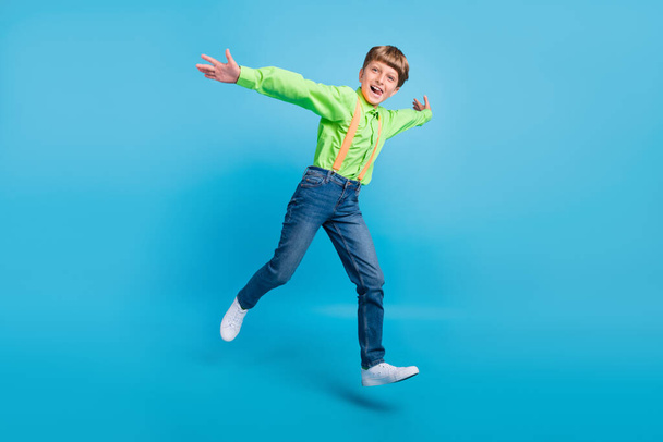 Full size photo of positive cheerful active small boy jump up enjoy weekend smile isolated on blue color background - Фото, изображение