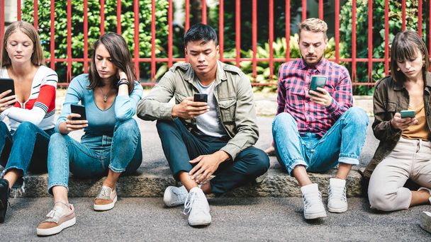 Milenijna grupa przyjaciół korzystająca ze smartfona siedzącego na podwórku koledżu uniwersyteckiego - Młodzi ludzie uzależnieni od smartfona - Koncepcja technologii z zawsze połączonymi studentami - Zdesperowany filtr - Zdjęcie, obraz