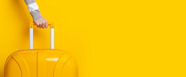 Kadın eli parlak sarı bir arka planda sarı bir bavulu tutuyor. Pankart. - Fotoğraf, Görsel