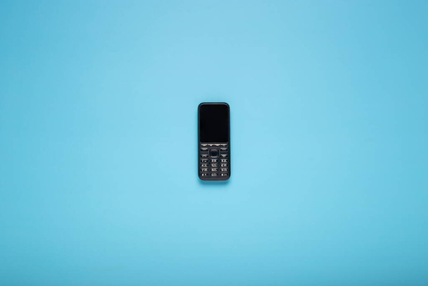 Old push-button mobile phone on a blue background. Top view, flat lay. - Fotografie, Obrázek