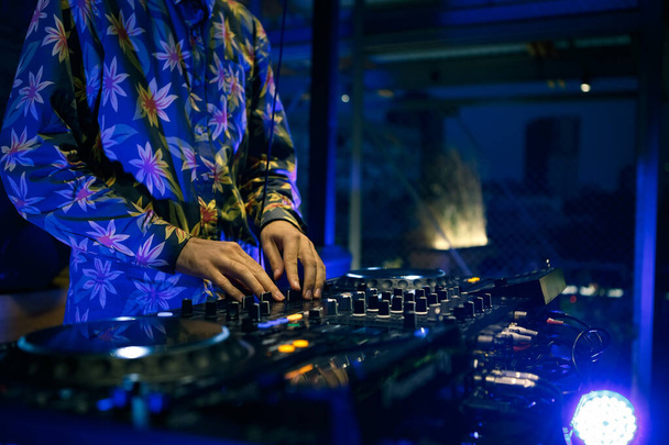 Techno dj playing musical tracks on stage in blue neon lights. Professional disc jockey plays electronic music on concert scene using sound mixer and turntables - Foto, afbeelding