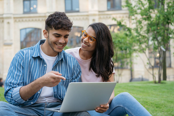 Lächelnde gemischte Rassenstudenten, die Laptop-Computer benutzen, Sprache lernen, Online-Bildungskonzept. Schöner indischer Mann und schöne afroamerikanische Frau arbeiten zusammen, selektiver Fokus  - Foto, Bild