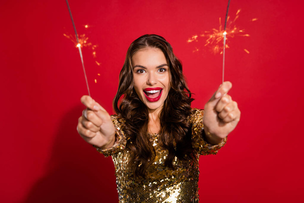 Photo of crazy excited lady hold two sparkling fire sticks wear golden dress isolated red color background - Foto, afbeelding