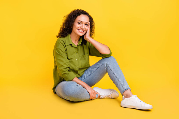 Photo of charming dreamy sweet woman dressed green shirt sitting floor arm cheek smiling isolated yellow color background - Photo, Image