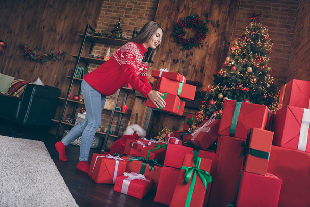 Photo of adorable pretty young woman dressed red sweater putting gifts under new year tree smiling indoors room home house - Photo, image