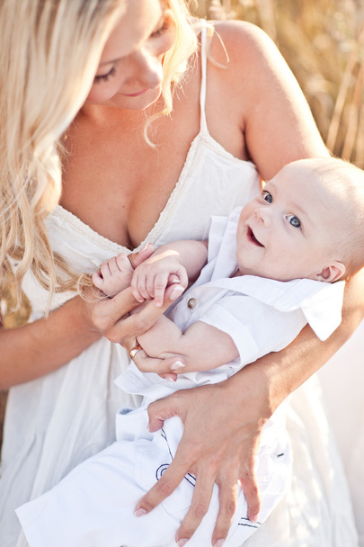 Familia feliz al atardecer. Madre en vestido blanco con bebé en la naturaleza
 - Foto, imagen