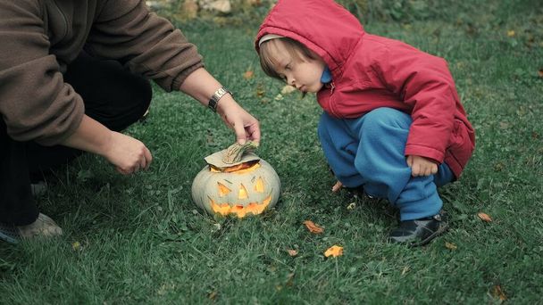 Mom and a cute little girl are lighting candles inside a pumpkin for Halloween - Photo, Image