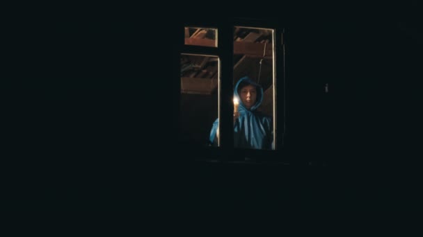 Woman in raincoat in attic of house. She gives signal with candle from window - Footage, Video