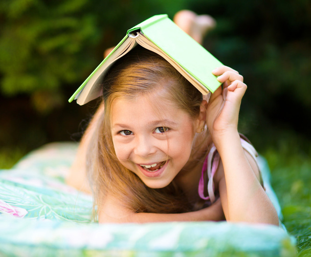 klein meisje is verstopt onder boek buitenshuis - Foto, afbeelding