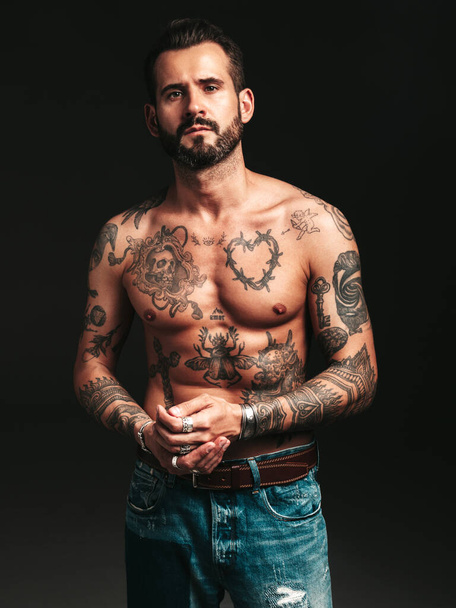 Portrait of handsome confident stylish hipster lambersexual model. Sexy modern man. Naked torso with tattoos.Fashion male posing in studio on dark background - Foto, afbeelding