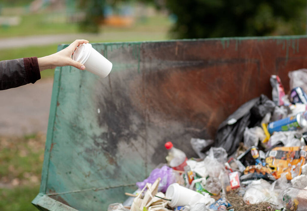 Kobieta wyrzucająca kartonowe szkło do kosza na śmieci. Dbanie o czystość miasta i środowiska. Duży kosz na śmieci w parku publicznym - Zdjęcie, obraz