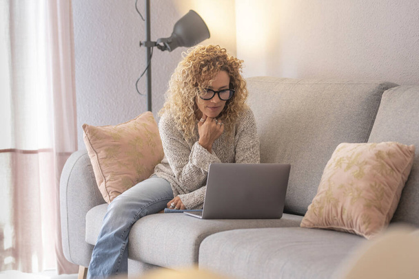 Mladá žena pracující na notebooku sedí na pohovce v obývacím pokoji doma. - Fotografie, Obrázek