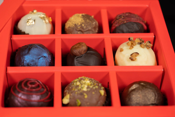 Koyu arkaplanda kırmızı bir kutuda çeşitli el yapımı çikolatalı şekerler. Görüntüyü kapat. - Fotoğraf, Görsel