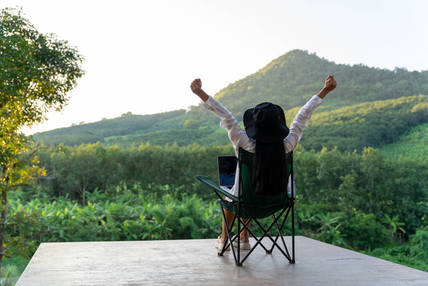 Een vrouw zit op een stoel genietend van vrijheid met open handen op de berg. - Foto, afbeelding