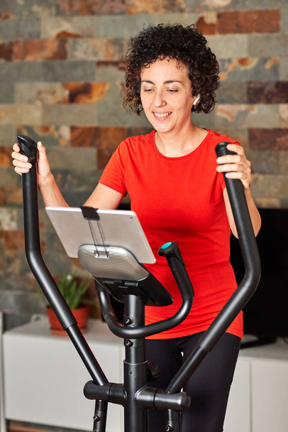 Nainen, joka treenaa kotona internetissä crosstrainingissa elliptisellä tunnilla - Valokuva, kuva