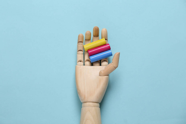 Wooden hand holds colored aa batteries on a blue background - Φωτογραφία, εικόνα