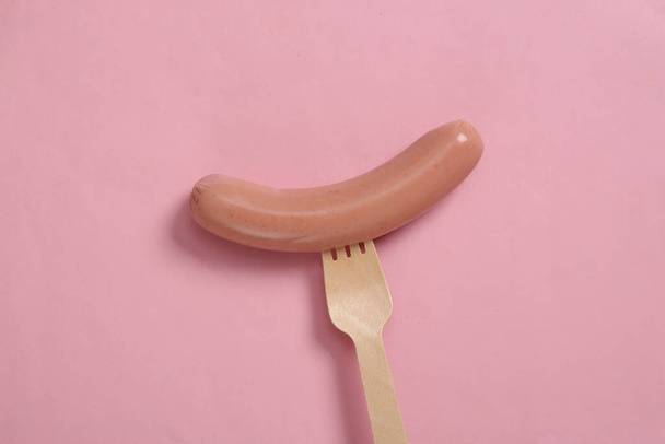Saucisse sur une fourchette en bois. Minimalisme alimentaire et concept écologique. Fond rose - Photo, image