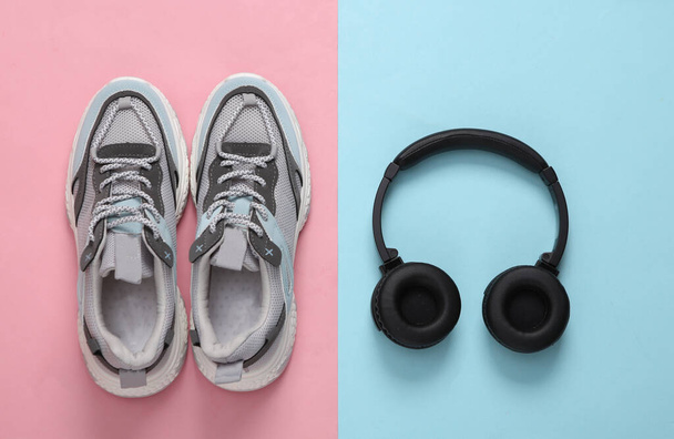 Sportovní boty a sluchátka na modrorůžovém pastelovém pozadí. Koncept fitness. Horní pohled. Minimalismus - Fotografie, Obrázek