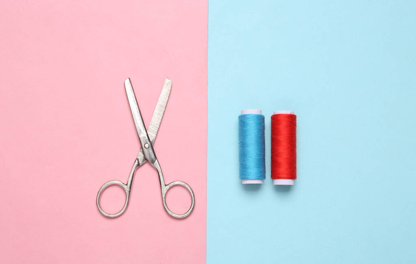 Skeins of colored thread and scissors on a blue-pink pastel background - Фото, изображение