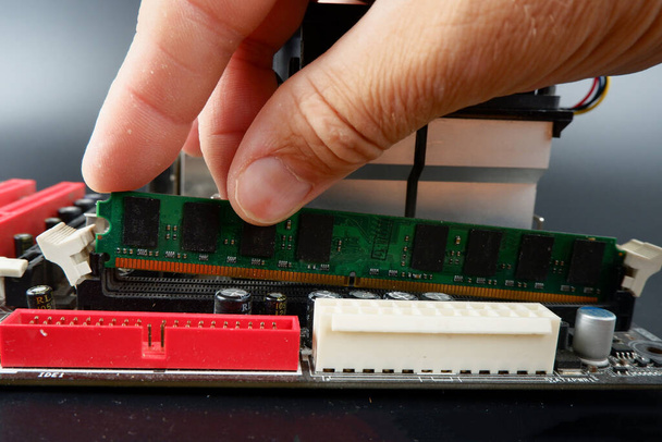κάποιος εγκαθιστά RAM σε μια υποδοχή στη μητρική πλακέτα ενός προσωπικού υπολογιστή. - Φωτογραφία, εικόνα