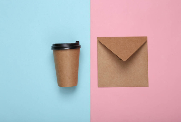 Craft envelope e xícara de café no fundo pastel azul-rosa. Vista superior - Foto, Imagem