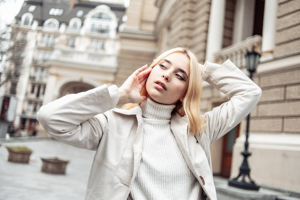 Portrait of a young fashion blonde woman in an autumn trench coat against the background of urban architecture - Fotoğraf, Görsel