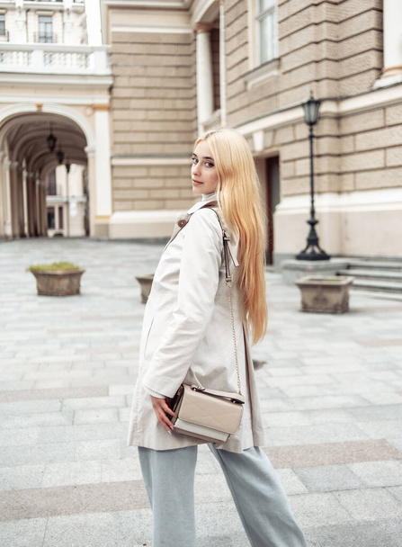 Портрет молодої блондинки в осінній траншеї пальто на тлі міської архітектури
 - Фото, зображення