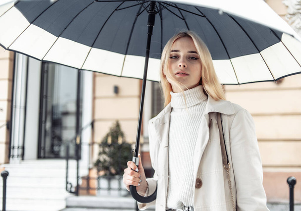 Jeune femme blonde en trench coat avec parapluie en ville - Photo, image