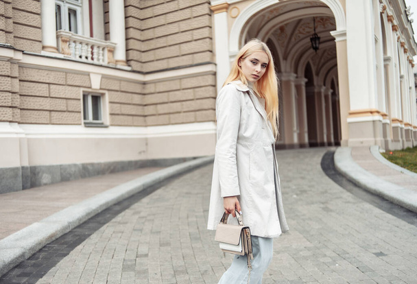 Молодая блондинка в пальто с сумкой в городе - Фото, изображение