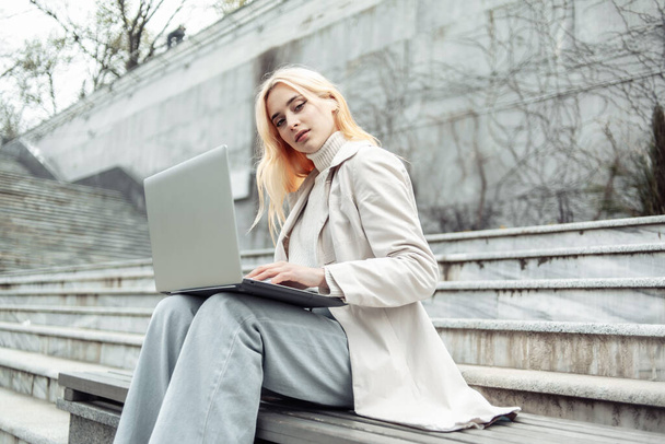 Young woman student uses a laptop while sitting on a bench on the background of the stairs - Foto, immagini