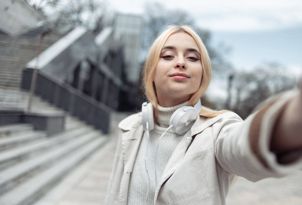 Young stylish girl with headphones makes selfie outdoors - Photo, Image