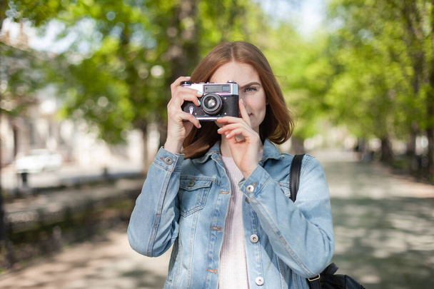 Roztomilá mladá atraktivní žena turista v džínové bundě s retro kamerou ve městě - Fotografie, Obrázek